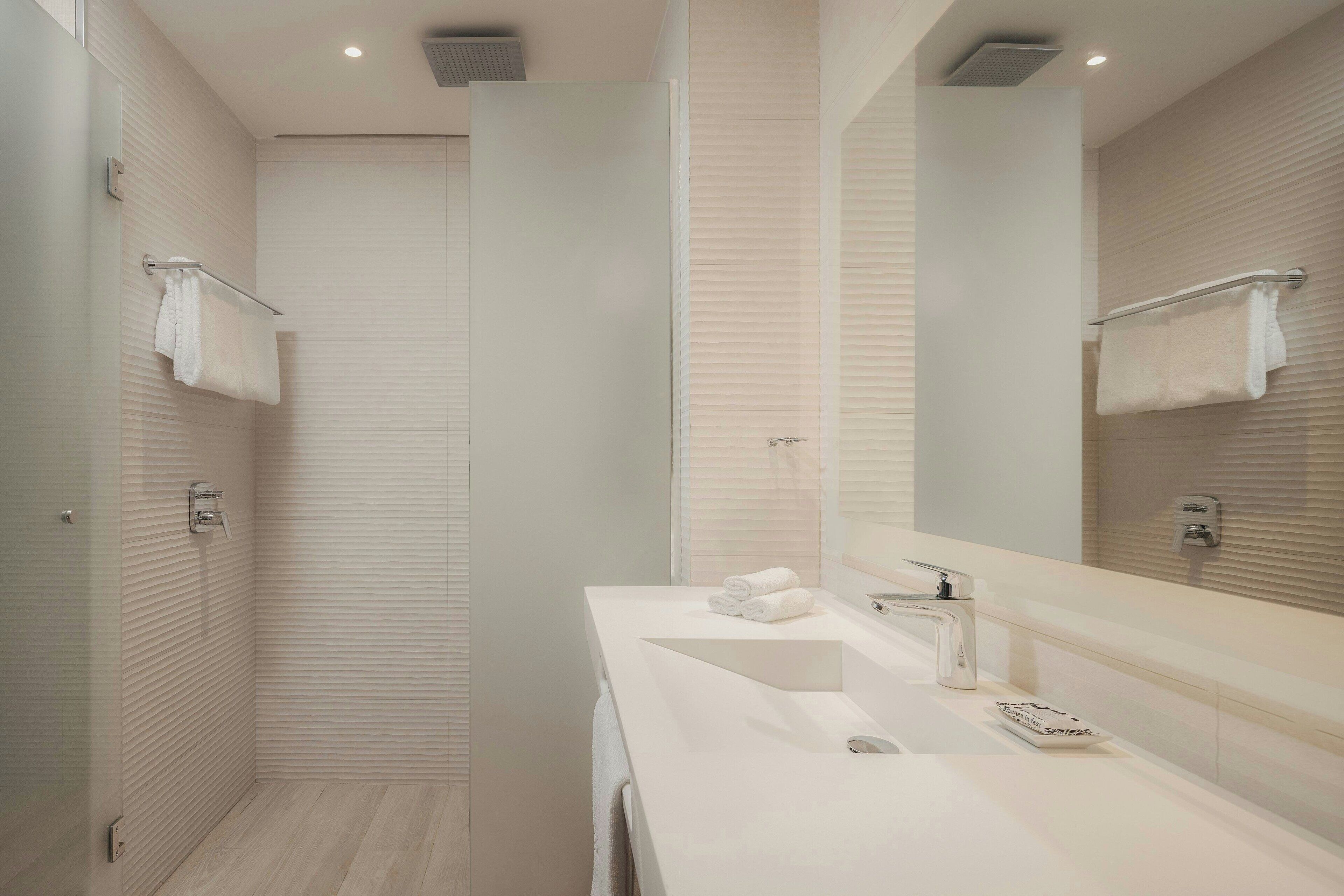 A modern bathroom with a walk-in shower, a large mirror, and a white sink.
