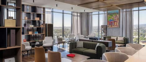 A modern living room with a city view, featuring a green sofa, white chairs, and a wooden coffee table.