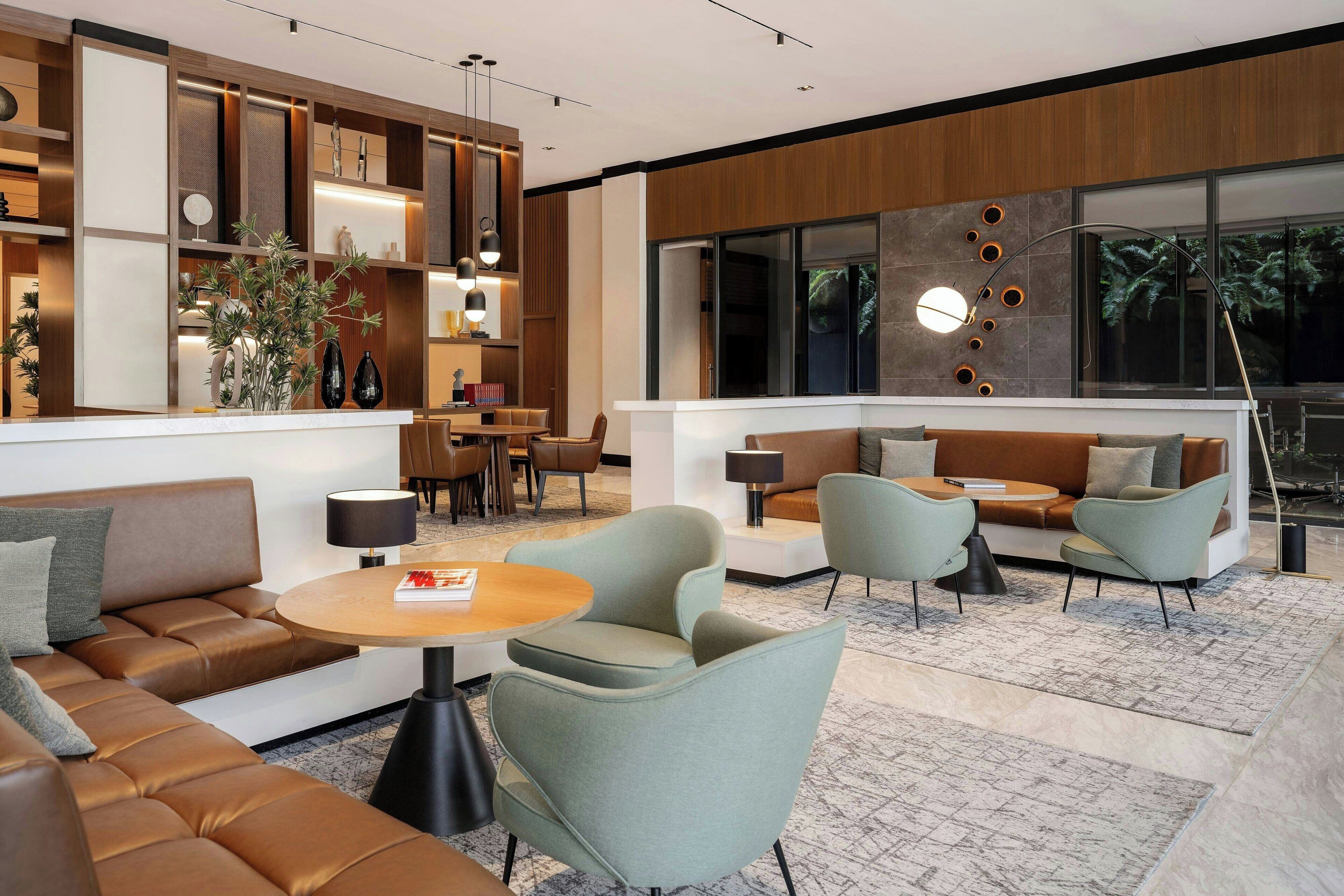Un vestíbul d'hotel modern amb zona de seients, una recepció i un gran finestral amb vista a arbres.