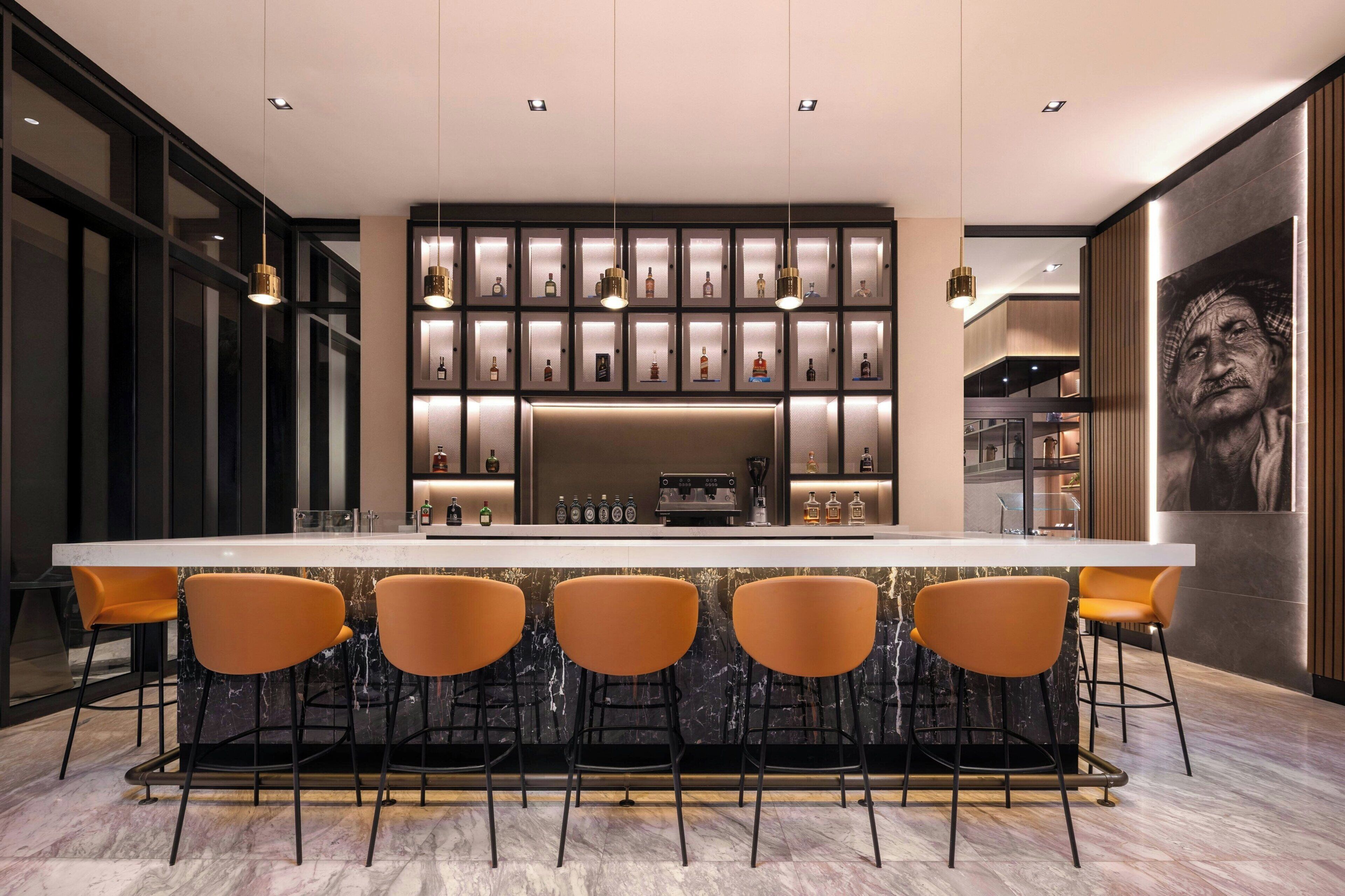 Un área de bar moderna con encimera de mármol, cuatro taburetes y una exhibición de botellas de licor.