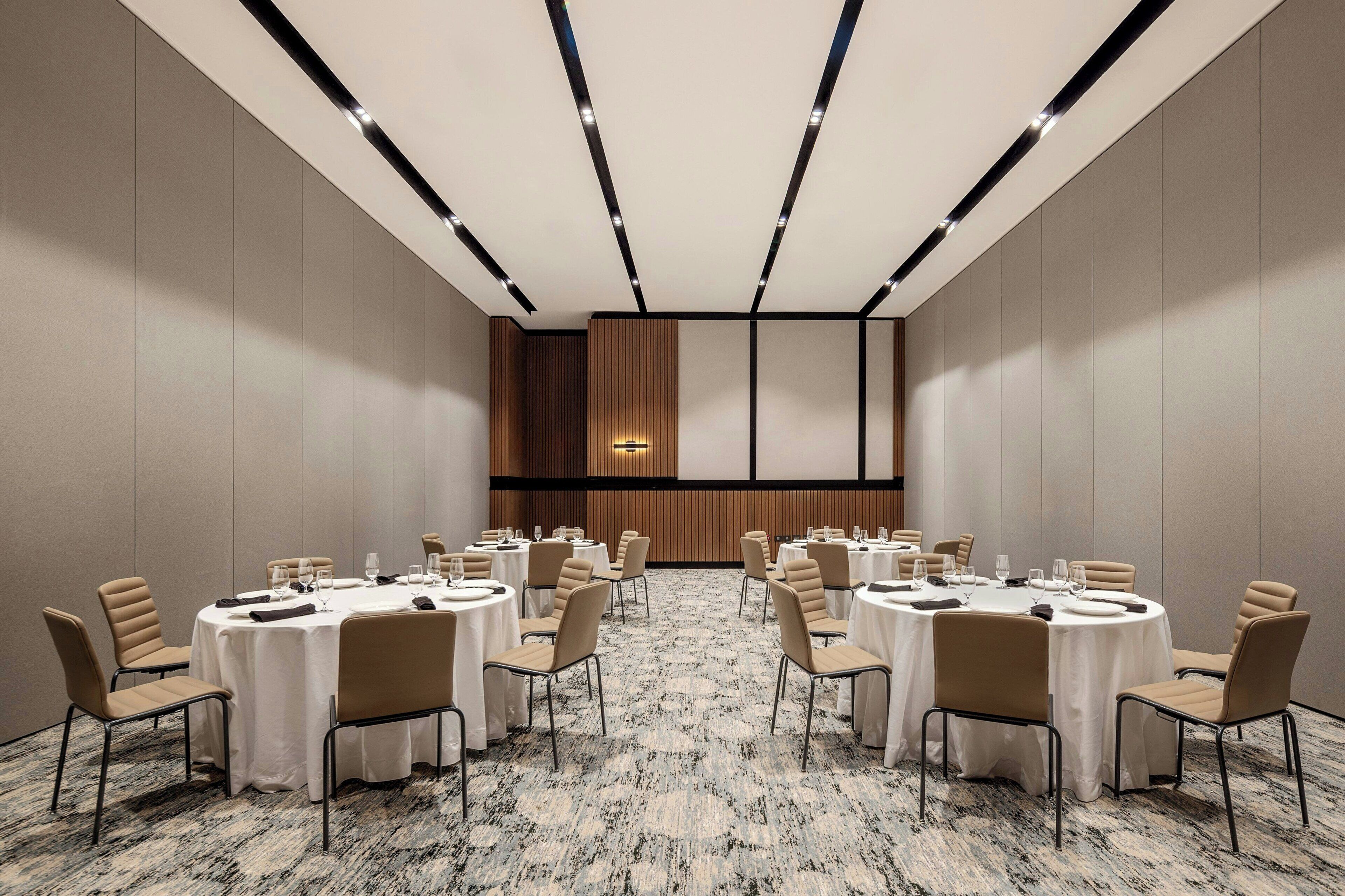 A conference room with round tables and chairs, a patterned carpet, and recessed lighting.