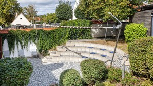 A courtyard with a curved seating area, stone pathway, and surrounding greenery. - "Designloft Thierhaupten - Creative retreat & Maisonette house " (Thierhaupten)
