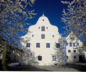 A white building with a cross on top, surrounded by blooming trees. - "Designloft Thierhaupten - Creative retreat & Maisonette house " (Thierhaupten)