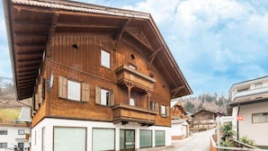 A traditional wooden chalet with a sloped roof, multiple windows, and a balcony.