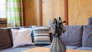 A modern living room with a grey sofa, striped pillows, and a grey vase with dried flowers on a wooden coffee table.