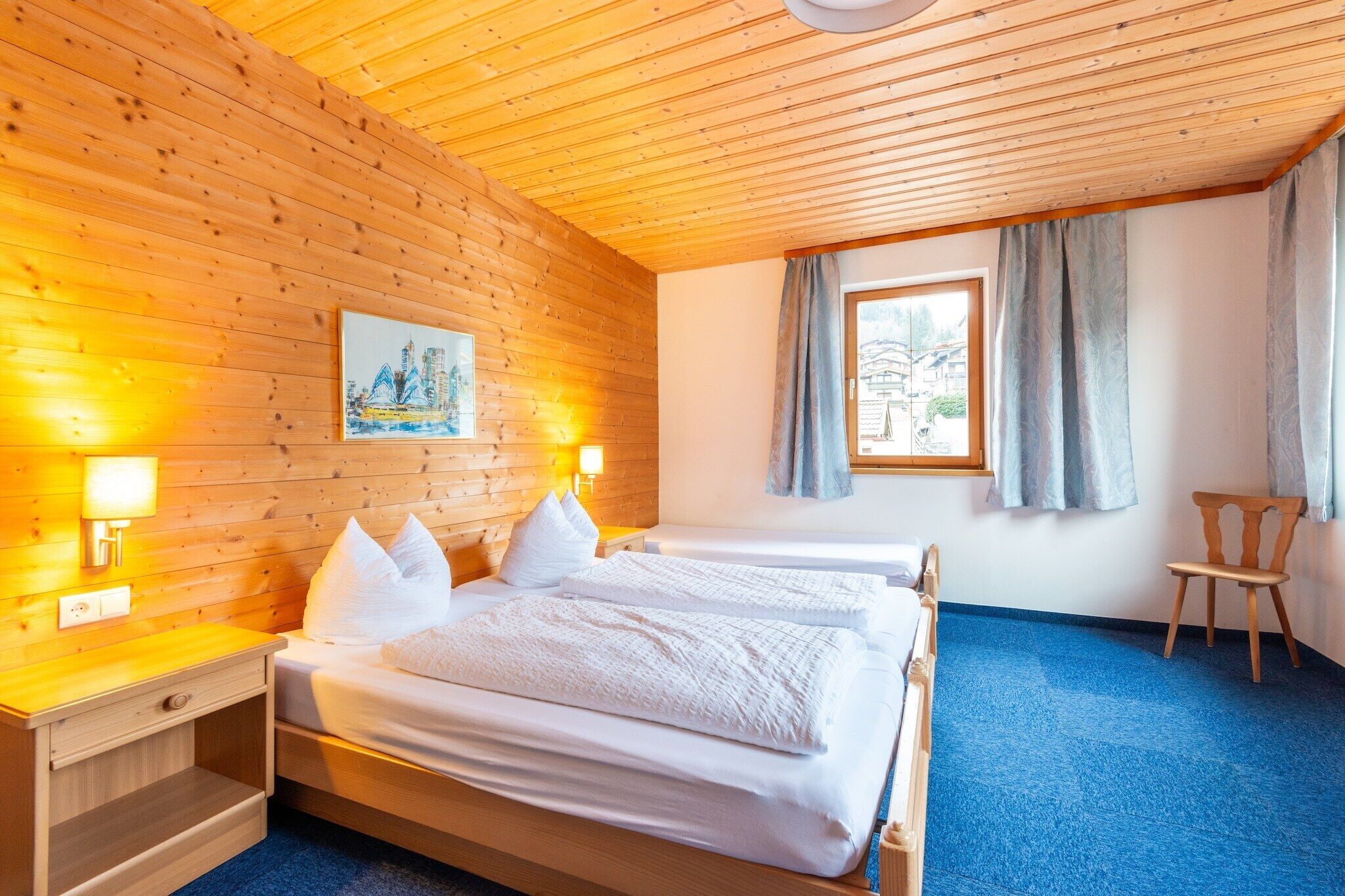 Een hotelkamer met houten wanden, twee bedden, een raam met gordijnen en een schilderij aan de muur.