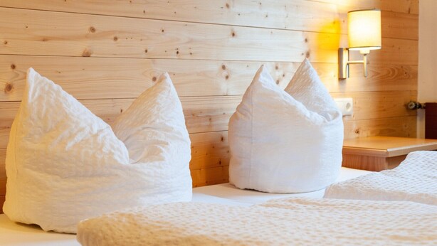 A room with a wooden wall, a bedside lamp, and two large, white, textured pillows.
