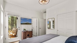 A bedroom with a large bed, a door leading to a balcony, a dresser, a television, and a mirror.