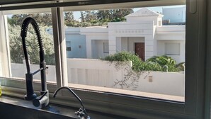 Una cocina con un lavamanos, grifo y ventana con vistas a una zona residencial.