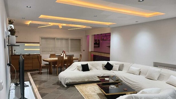 Una sala de estar moderna con un sofá blanco, una mesa de centro y un televisor. Hay un comedor con una mesa y sillas.