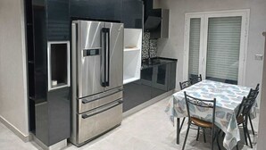 Una cocina moderna con refrigerador integrado, una mesa de comedor con sillas y una ventana con persianas.