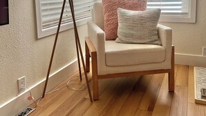 Een gezellig hoekje met een beige fauteuil, een vloerlamp en een raam met jaloezieën.