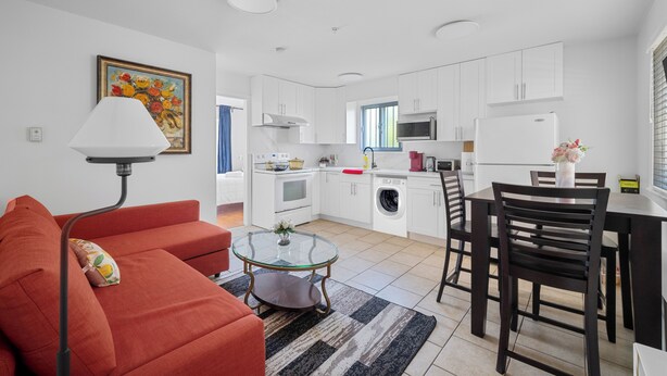 A modern kitchen with white cabinets, a dining table, and a red sofa. - Lovely ground floor suite in Central Vancouver (Vancouver)