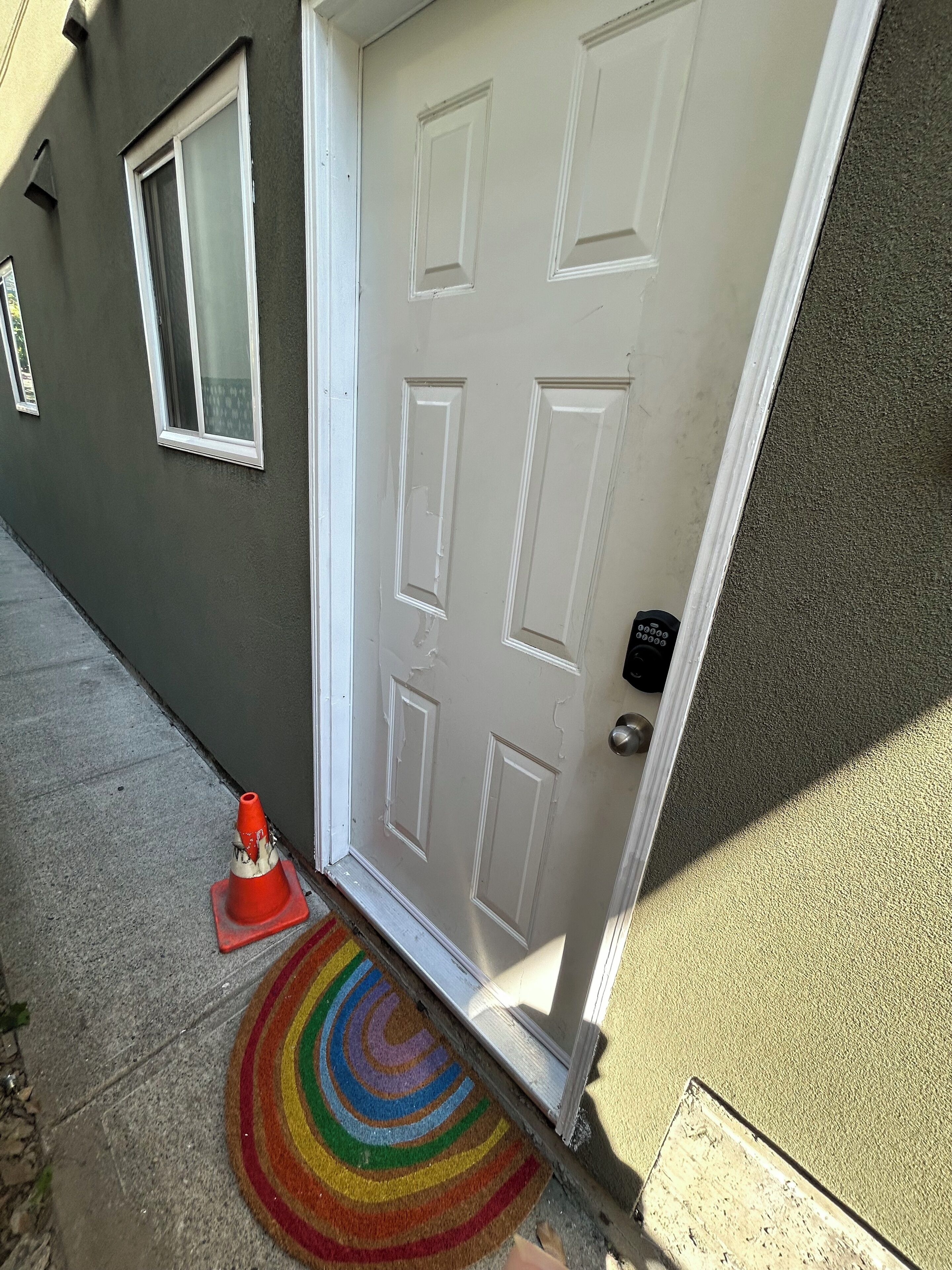 A white door with a keypad lock, a red traffic cone, and a colorful circular rug on the ground.