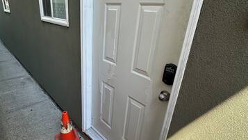 A white door with a keypad lock, a red traffic cone, and a colorful circular rug on the ground.