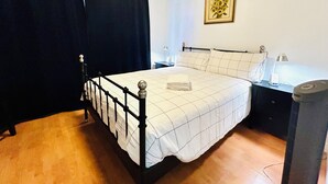 A bedroom with a bed, a nightstand, a lamp, a picture frame, and a heater. - Lovely ground floor suite in Central Vancouver (Vancouver)