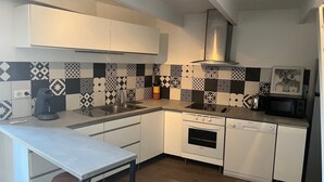 Ett modernt kök med vita skåp, ett svart- och vitmönstrat stänkskydd, en rostfri köksfläkt, en mikrovågsugn och en diskmaskin.