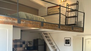 En lägenhet i loftstil med kök, matplats och en trappa som leder upp till en sovplats på entresolplan.