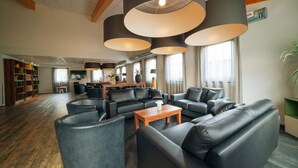 A spacious living room with leather sofas, a wooden coffee table, and large pendant lights. - Holiday home for group with sauna and pool (Havelte)