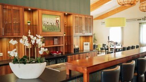 A modern kitchen with wooden cabinets, a large island with a white bowl of flowers, and a clock on the wall. - Holiday home for group with sauna and pool (Havelte)