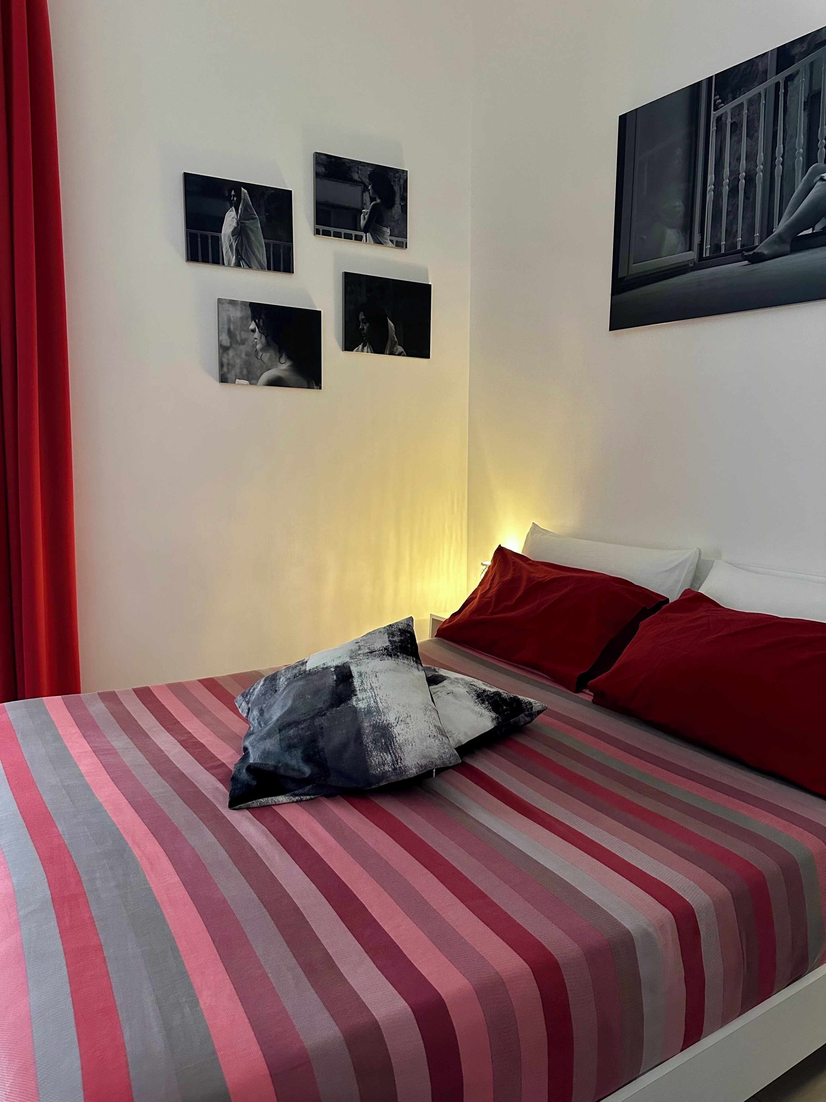 A bedroom with a striped bedspread, a red pillow, and a wall with four framed pictures.