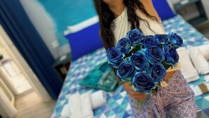A person holding a bouquet of blue roses in a room with a bed, pillows, and a blue and white checkered bedspread. - Napoli Museo Bed and Breakfast (Naples)
