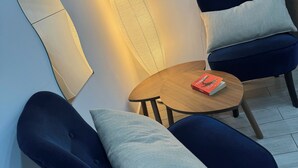 A modern room with a round wooden table, two dark blue chairs with light grey cushions, a small TV mounted on the wall, and a patterned wall lamp. - Napoli Museo Bed and Breakfast (Naples)