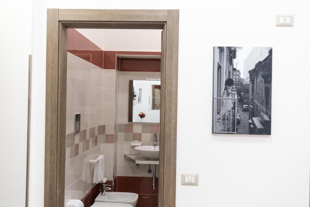 A bathroom with a wooden door, a sink, a mirror, and a toilet. There is a framed picture on the wall.