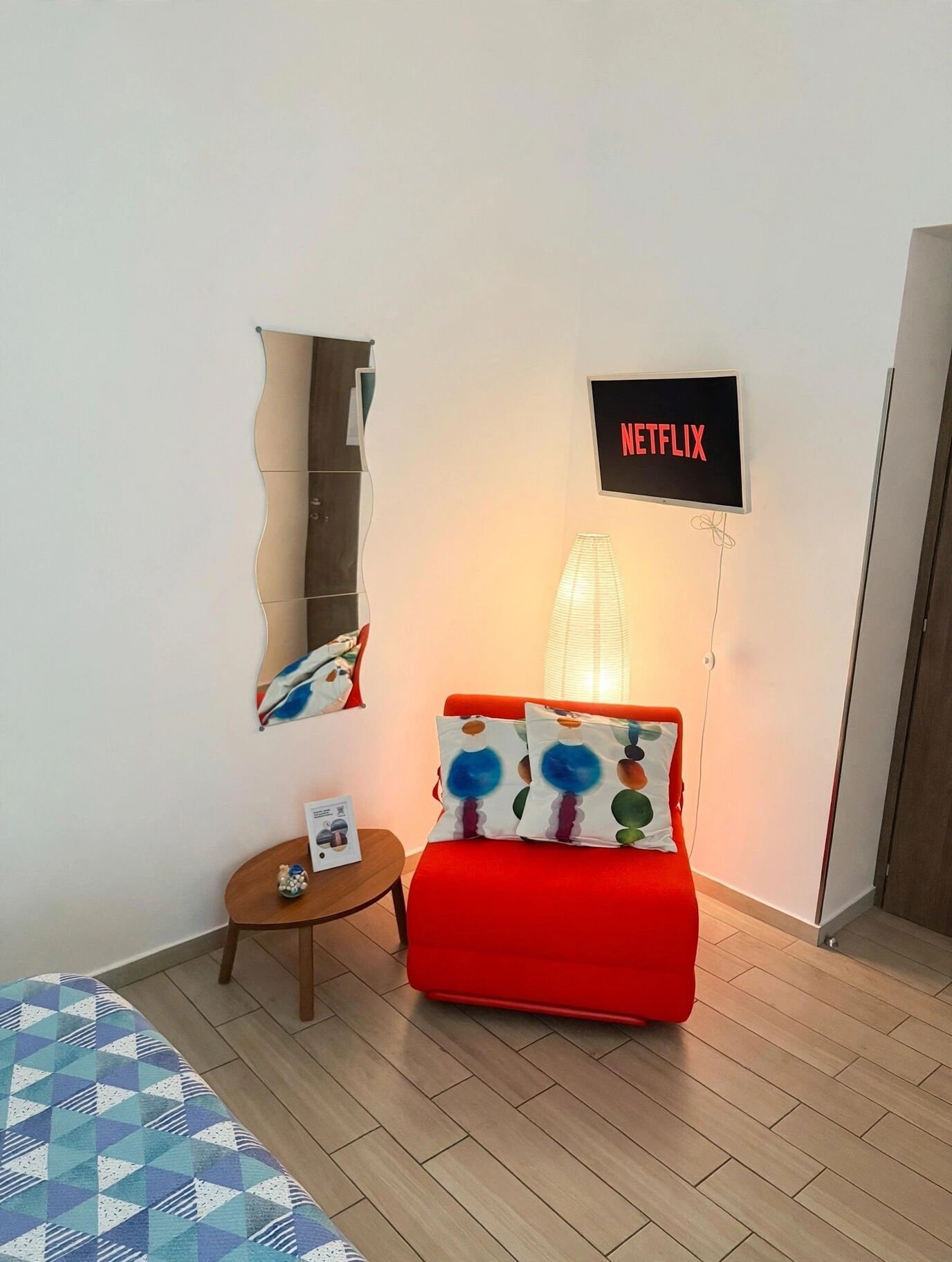 A room with a red sofa, a small side table, a wall-mounted shelf, and a wall-mounted sign that reads 'NETFLIX'.