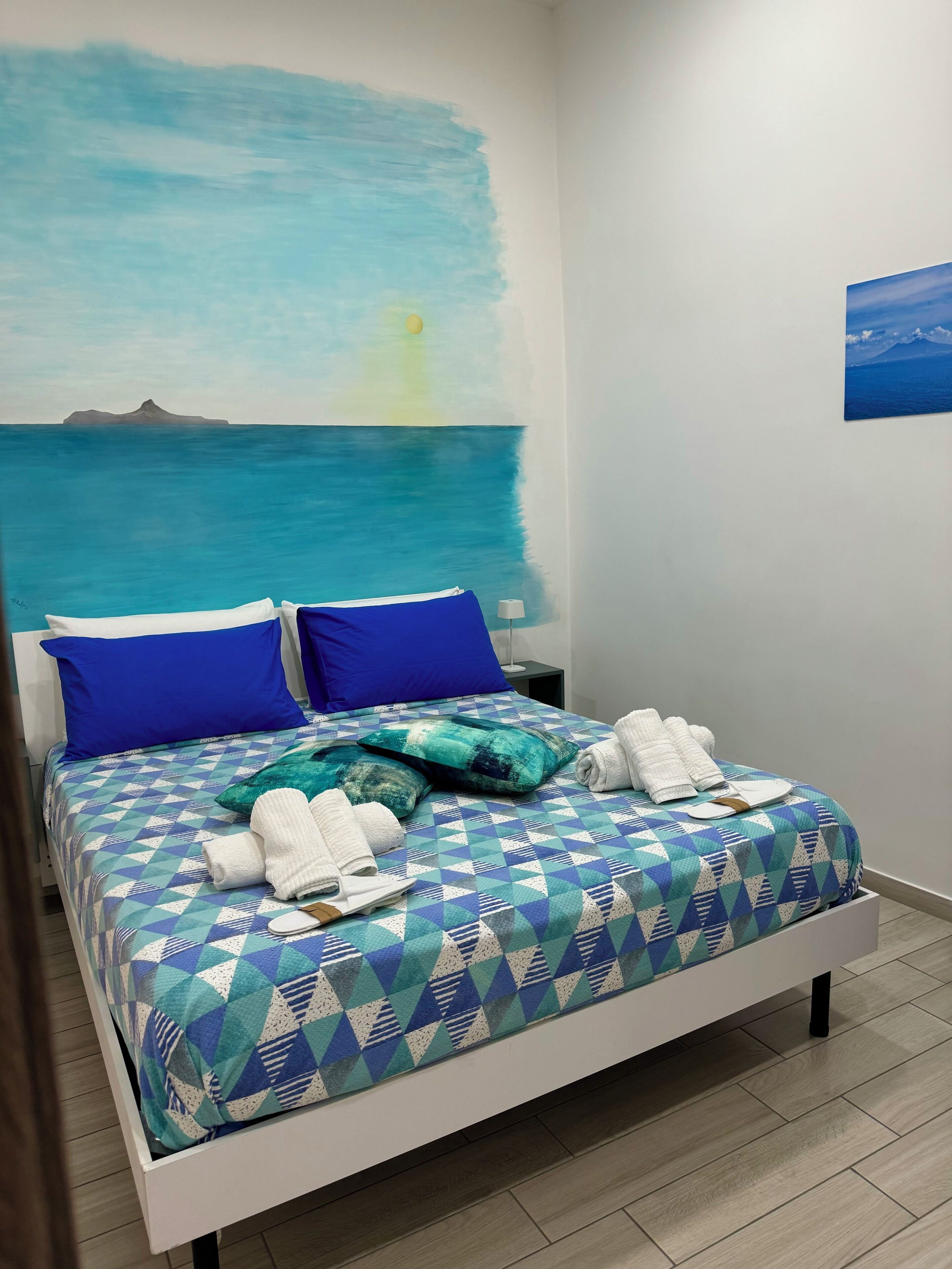 A bed with a geometric patterned bedspread, two blue pillows, and a teal throw blanket.