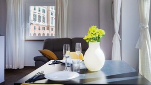 A hotel room with a dining table set for two, a vase with yellow flowers, and a view of buildings through a window. - San Lorenzo View by Wonderful Italy (Genoa)