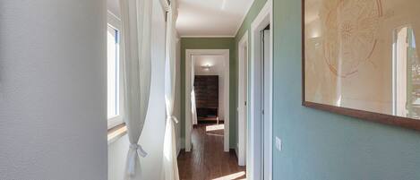 A hallway with wooden flooring, white curtains, and a framed map on the wall.