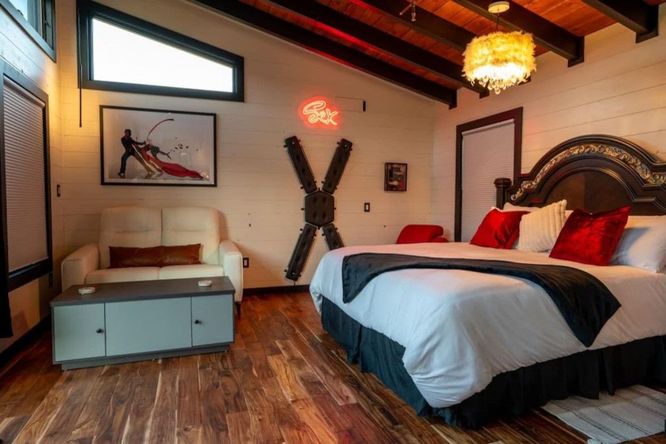 A bedroom with a bed, a desk, a chair, a neon sign, and a unique wall decoration.
