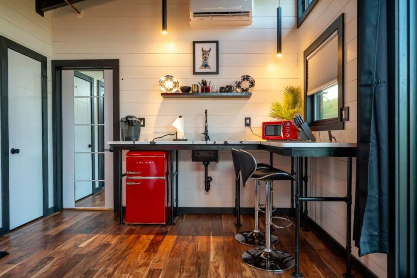 A compact kitchen with a red refrigerator, a sink, a microwave, and a bar stool.
