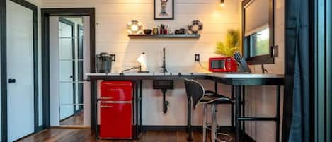 A compact kitchen with a red refrigerator, a sink, a microwave, and a bar stool.
