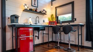Een compacte keuken met een rode koelkast, een magnetron en een spoelbak. Twee zwarte barkrukken en een raam met uitzicht op groen.