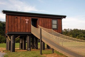 A wooden cabin with a rope slide leading to a window.