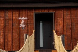 Une façade en bois, ornée d’une enseigne au néon indiquant « Ahaasia & Grey », et une barrière faite de cordes devant une porte sombre.