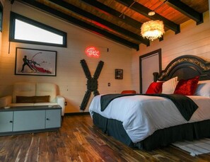 A bedroom with a bed, a nightstand, a dresser, a neon sign, and a framed picture on the wall.
