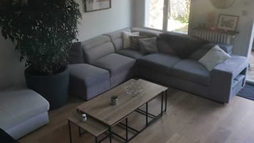 Ein modernes Wohnzimmer mit einem Ecksofa, einem Couchtisch und einer großen Topfpflanze.