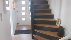 A staircase with wooden steps and a black handrail, leading to a door with a mirror and a framed picture on the wall. - The Crew House Amiens (Cagny)