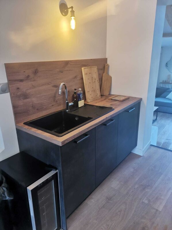 Ett modernt kök med en träpanel bakom arbetsbänken, svarta skåp, en svart bänkskiva, en diskho, en inbyggd diskmaskin och en väggmonterad lampa.