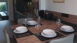 A dining area with a wooden table set for four, surrounded by chairs, and overhead pendant lighting. - The Crew House Amiens (Cagny)