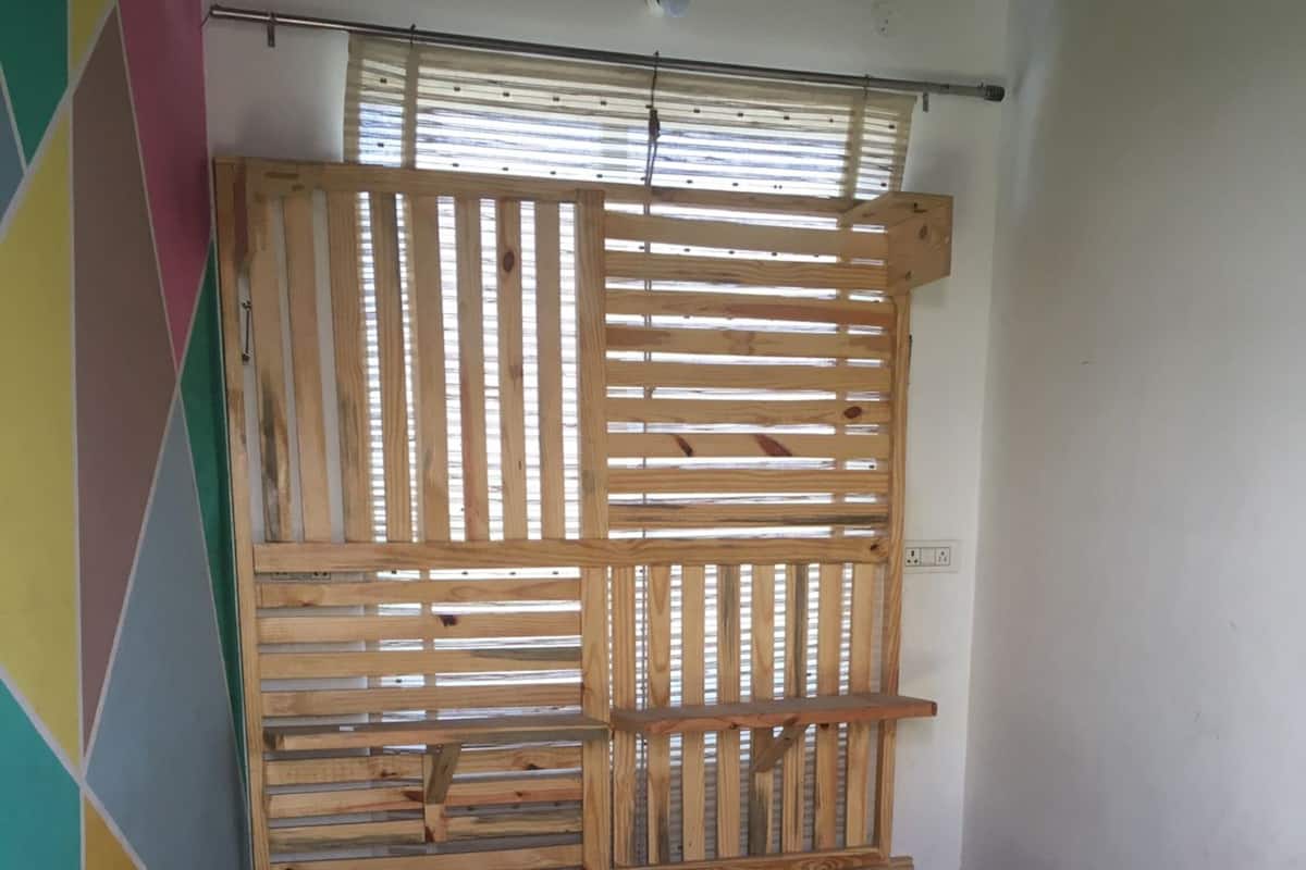 A room with a bed, a wooden slat headboard, a colorful wall, and a power outlet on the wall.