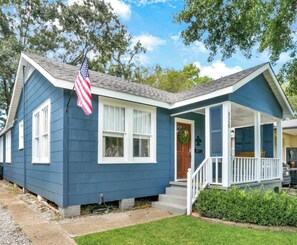 A single-story house with a front porch, a small front yard, and an American flag.