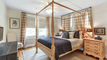 A four-poster bed with a ceiling fan, a bedside table with a lamp, and a dresser with drawers.
