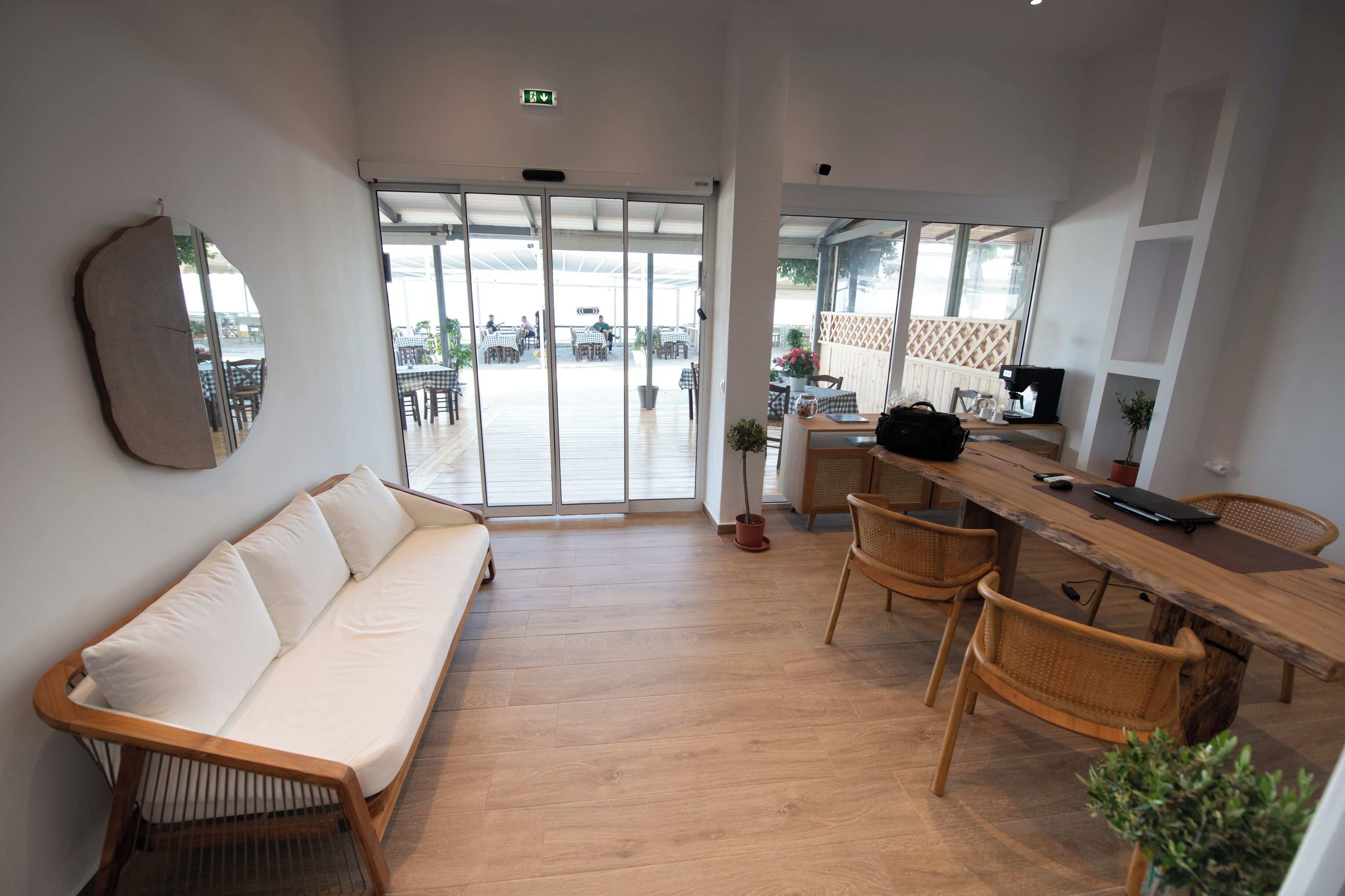 A modern interior with a wooden floor, a white sofa, a wooden table, wicker chairs, and a large window with a view of the outside.