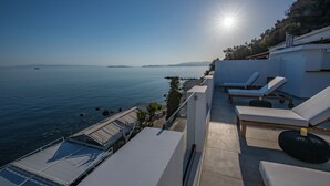 Eine Dachterrasse mit Blick auf das Meer, die Sonne und Liegestühle.