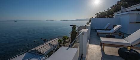 A rooftop terrace with a view of the sea, sun, and lounge chairs.