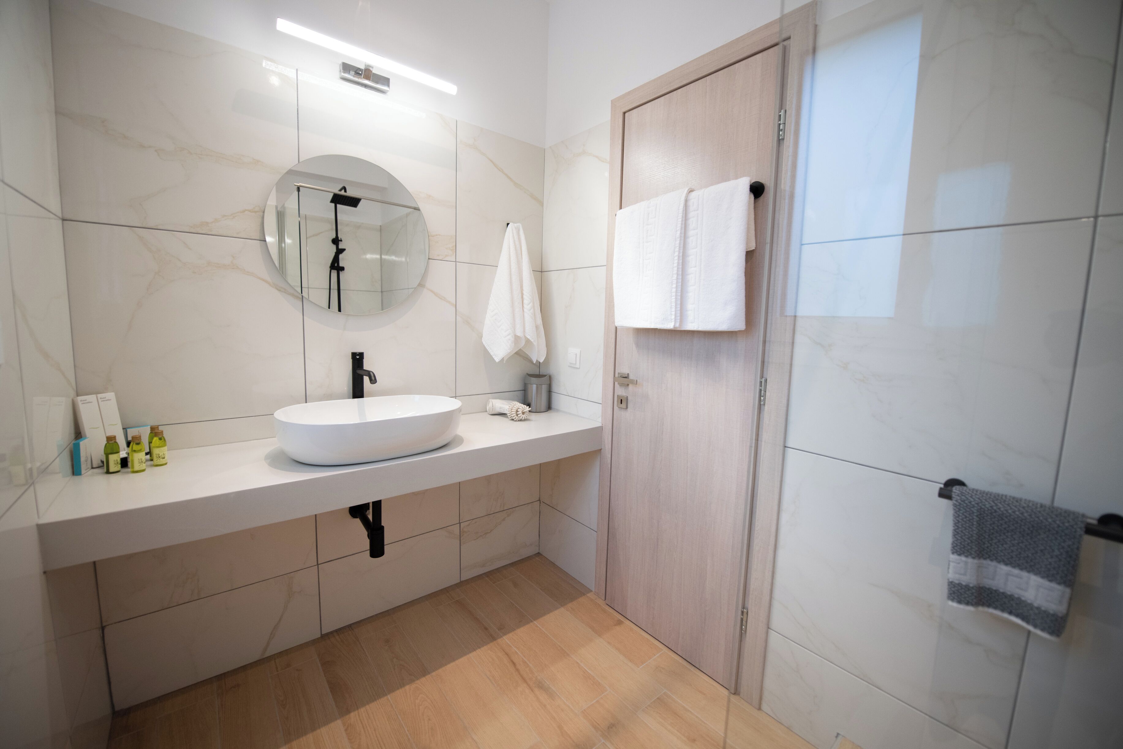 Een moderne badkamer met een ronde spiegel, een witte wastafel en een houten deur.